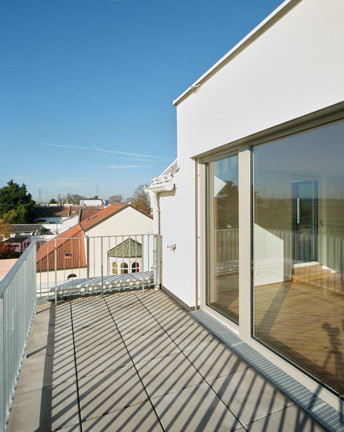 Sonniger Balkon mit Fliesenboden und Blick auf die umliegenden Dächer und den Himmel.