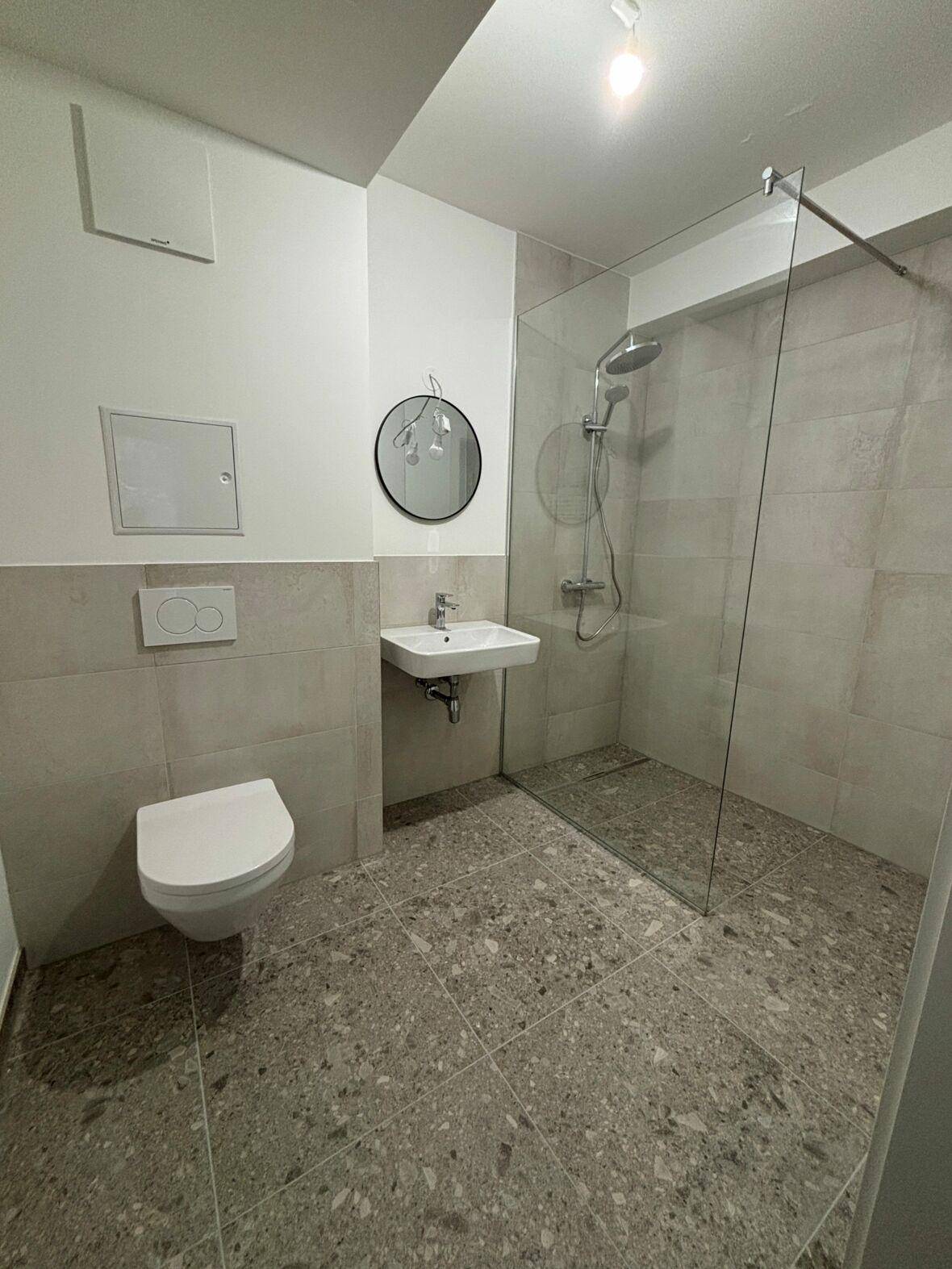 Modernes Badezimmer mit ebenerdiger Dusche, Hänge-WC und grauen Fliesen.