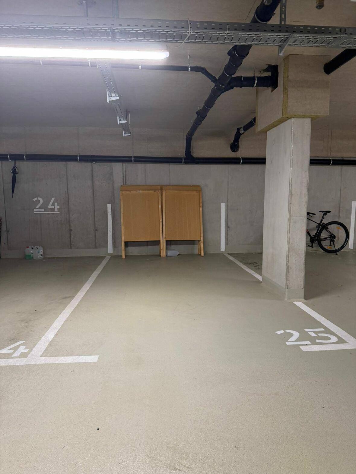 Heller Stellplatz in einer Tiefgarage mit sichtbaren Leitungen und einem Fahrrad.