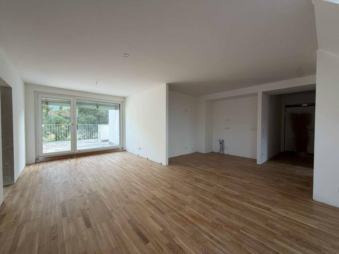 Geräumiges, helles Zimmer mit Parkettboden und großem Balkonzugang in einem Neubau.