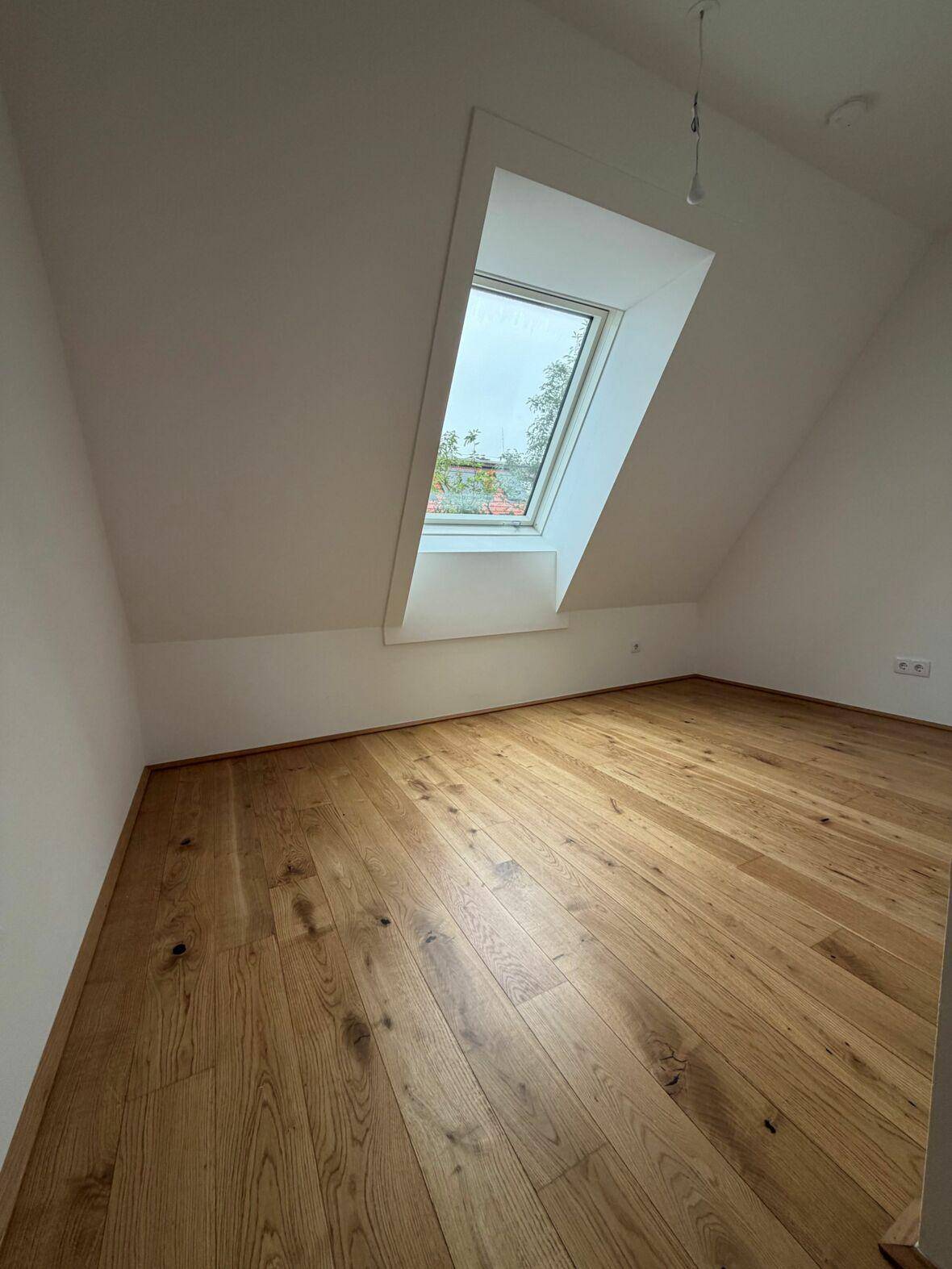 Geräumiges Dachgeschosszimmer mit warmem Echtholzboden und viel Tageslicht durch das große Dachfenster.