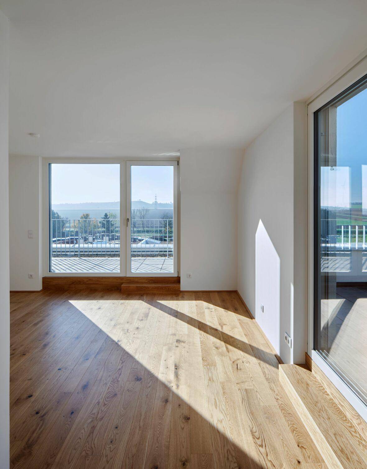 Helles Wohnzimmer mit Holzboden und großen Fenstern, die viel Tageslicht hereinlassen.