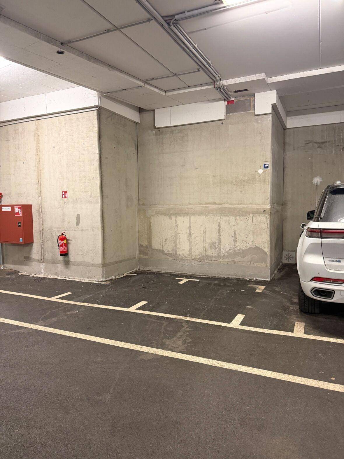 Leerer Tiefgaragenstellplatz mit Feuerlöscher und Betonwänden.