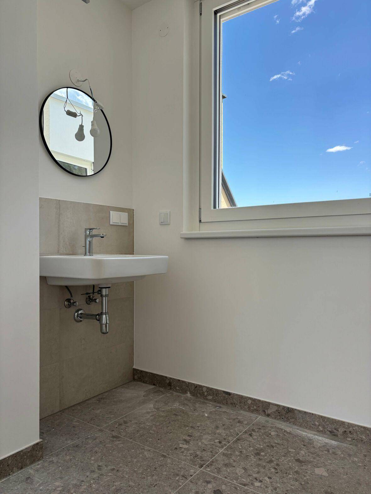 Modernes Gäste-WC mit Waschbecken, rundem Spiegel und Fenster für Tageslicht.
