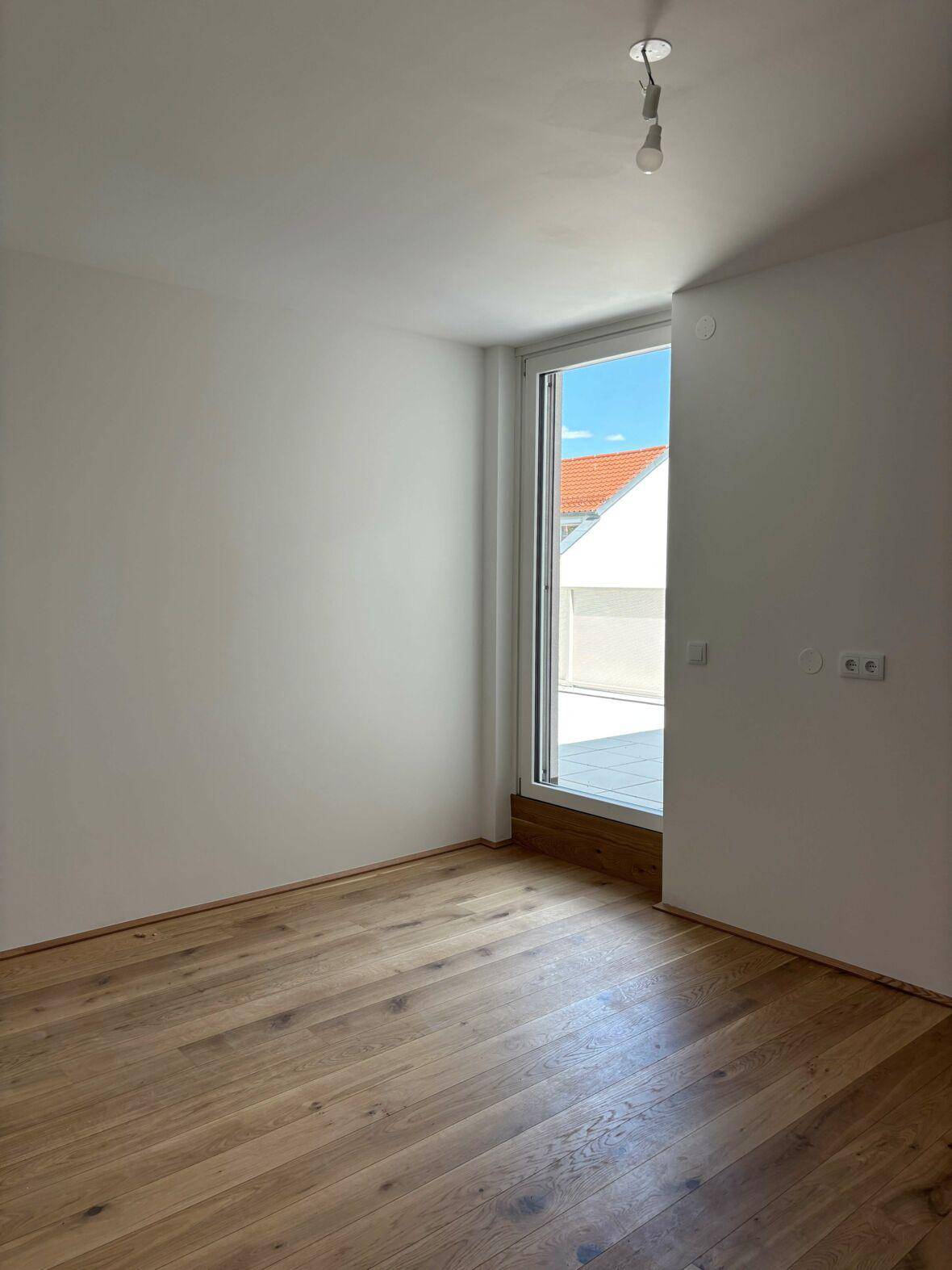 Leeres Zimmer mit Holzboden und Zugang zu einem Außenbereich, ideal als Schlafzimmer.