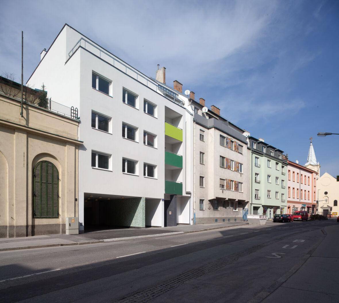 Moderne Wohngebäude mit Balkonen und einer Tiefgarageneinfahrt an einer städtischen Straße.