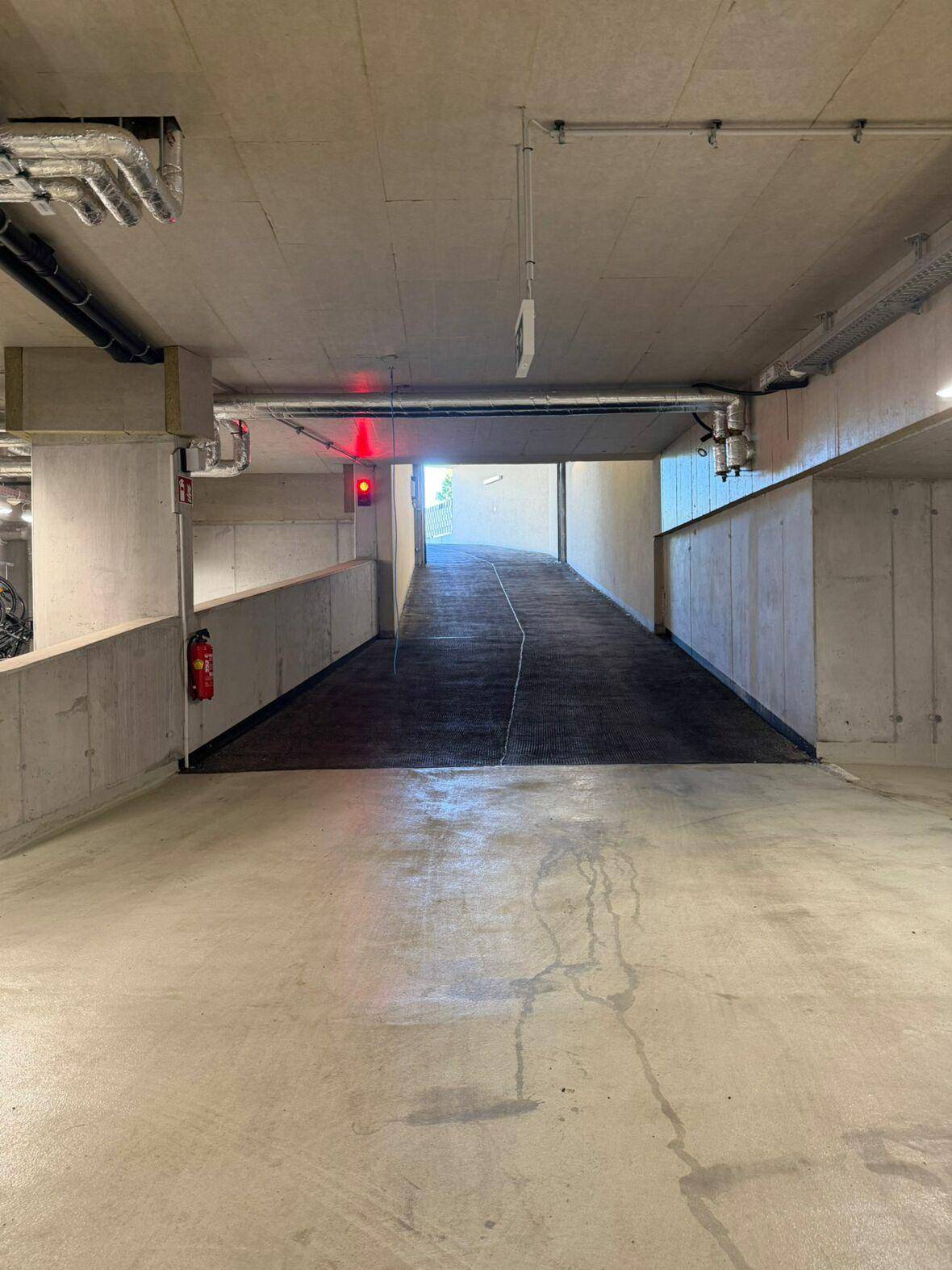 Einfahrt zu einer modernen Tiefgarage mit Betonwänden und heller Beleuchtung.