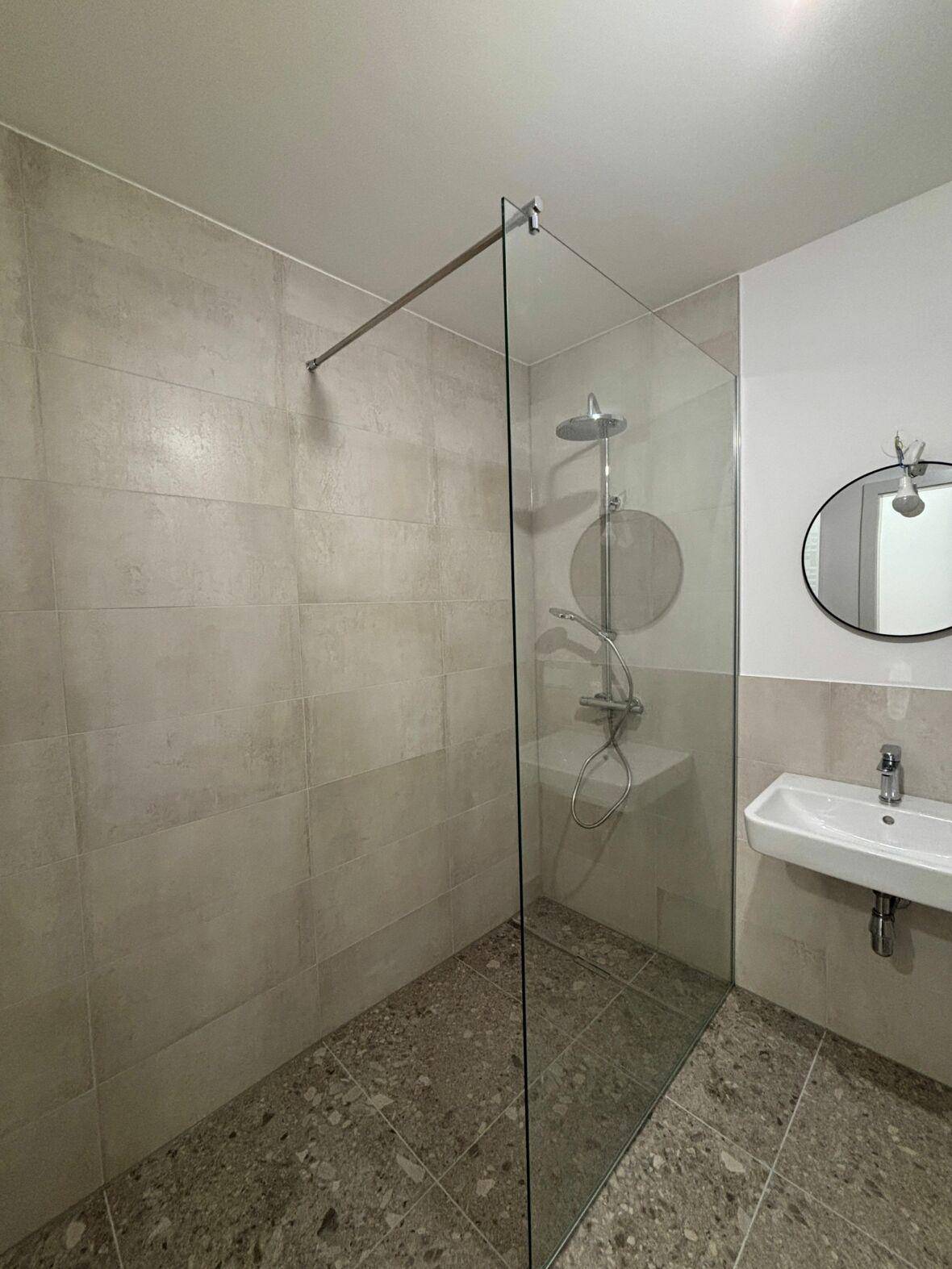Modernes Badezimmer mit ebenerdiger Dusche, hellen Fliesen und minimalistischem Waschbecken.