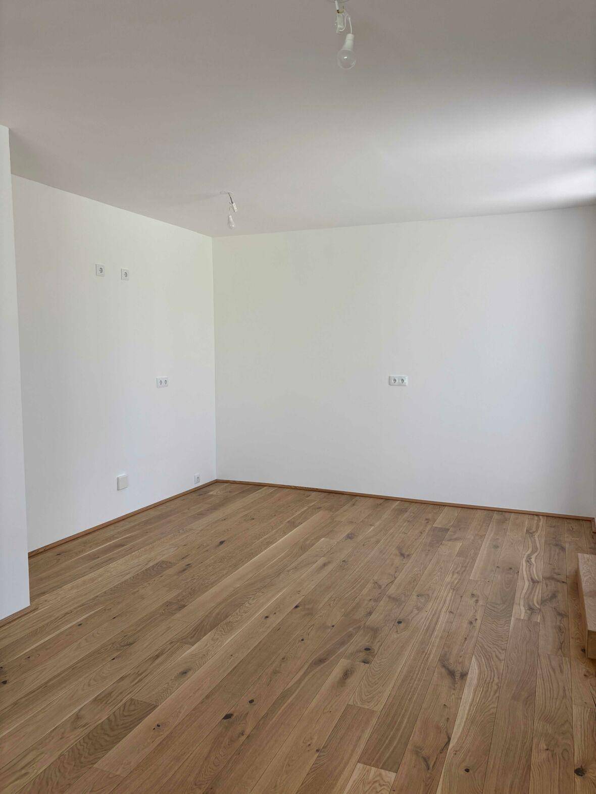 Heller, leerer Raum mit Holzboden und weißen Wänden, bereit zur individuellen Gestaltung.