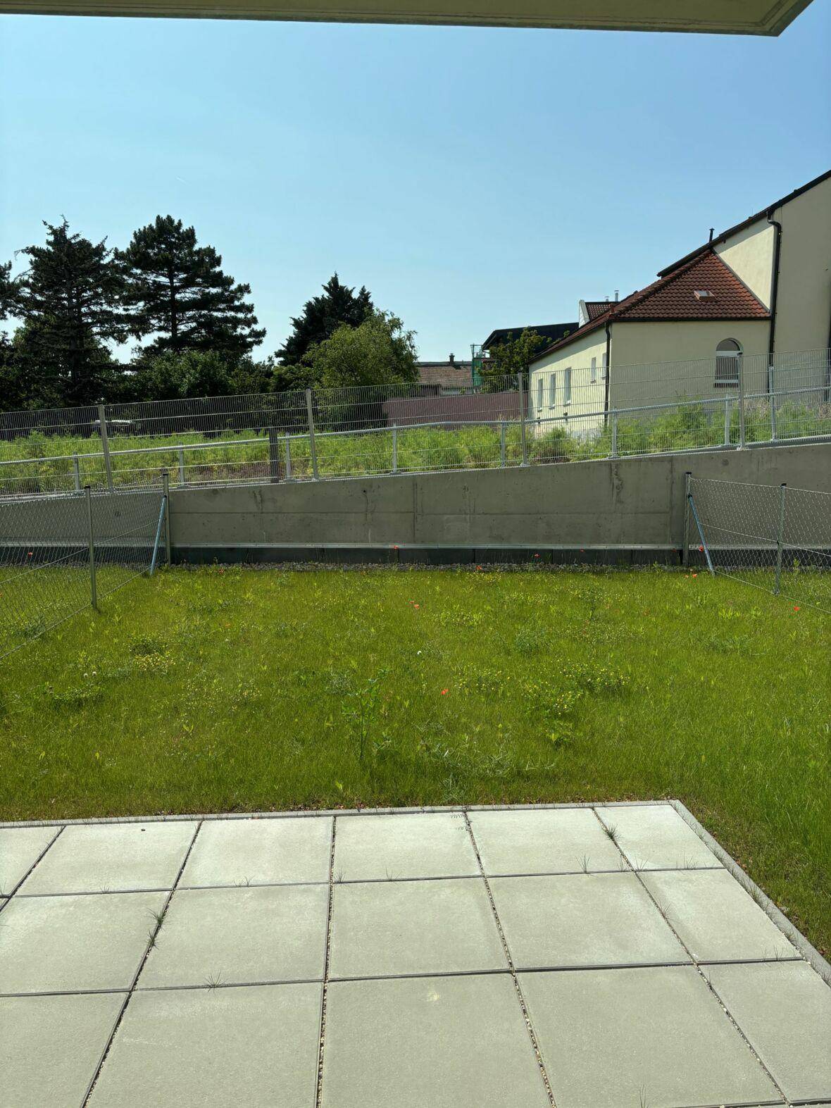 Außenbereich mit gefliester Terrasse und angrenzender Rasenfläche, umgeben von Grün.