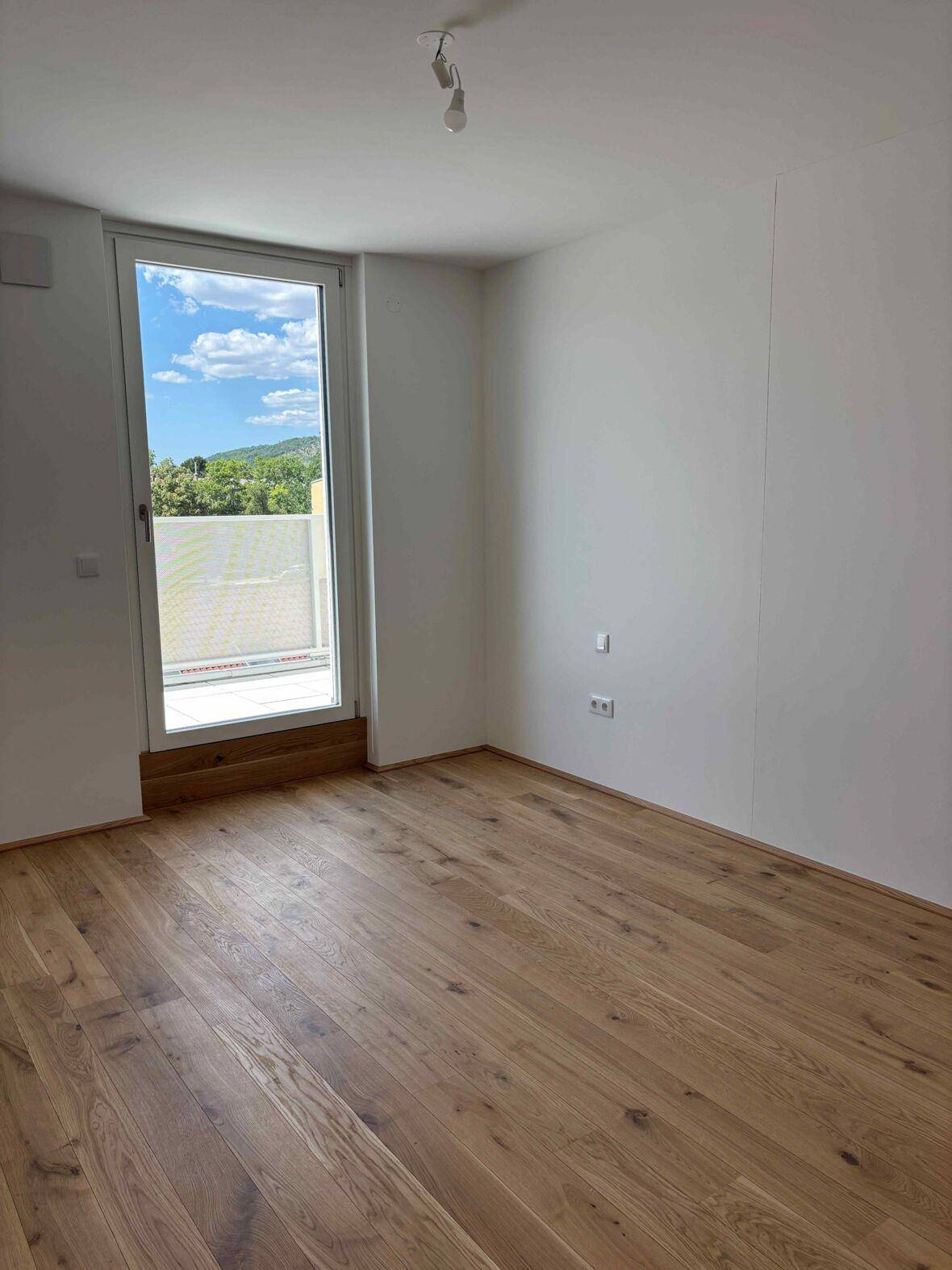 Helles Schlafzimmer mit Holzboden und Zugang zu einem Außenbereich, umgeben von Grün.
