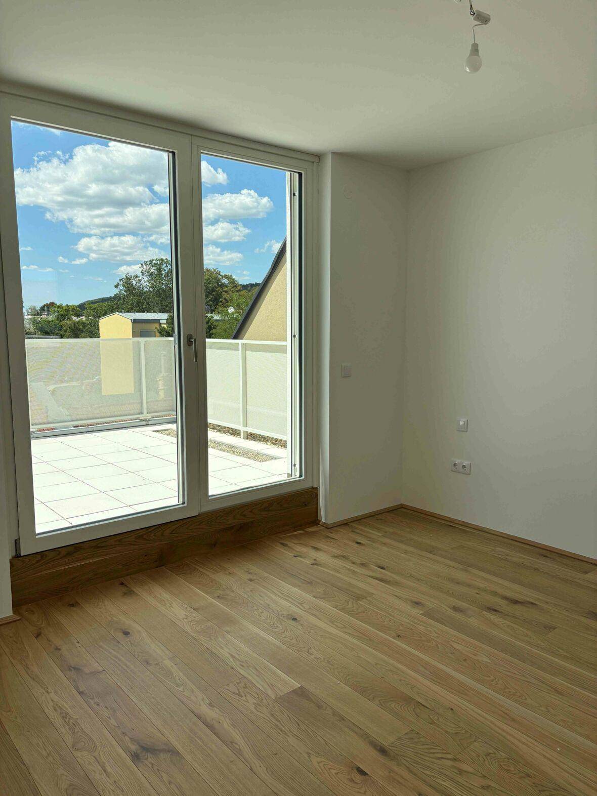 Lichtdurchflutetes Zimmer mit Holzboden und direktem Zugang zur sonnigen Terrasse.