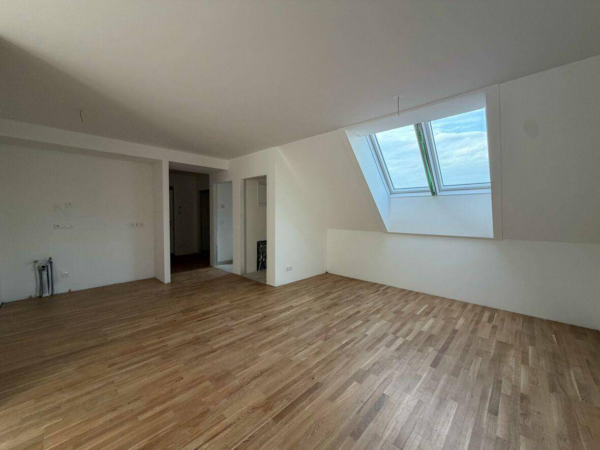 Geräumiges Zimmer mit Parkettboden, Dachschräge und zwei hellen Dachfenstern im Neubau.