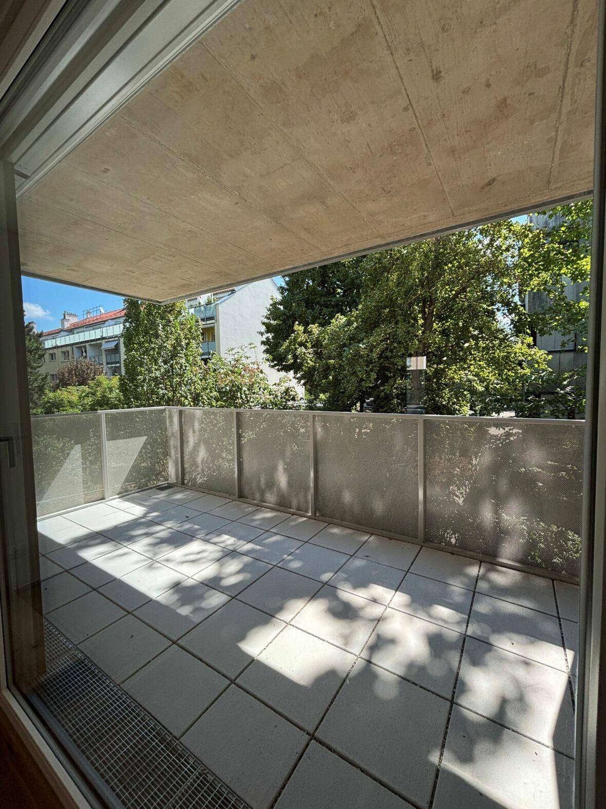 Geräumiger Balkon mit Fliesenboden und Blick auf grüne Bäume, ideal zum Entspannen im Freien.