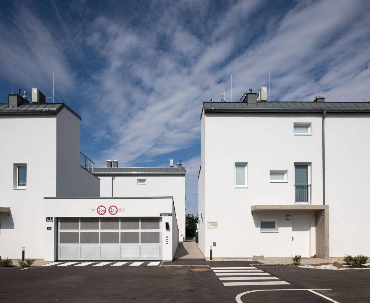 Moderne weiße Reihenhäuser mit Garagen und klarem Design unter blauem Himmel.