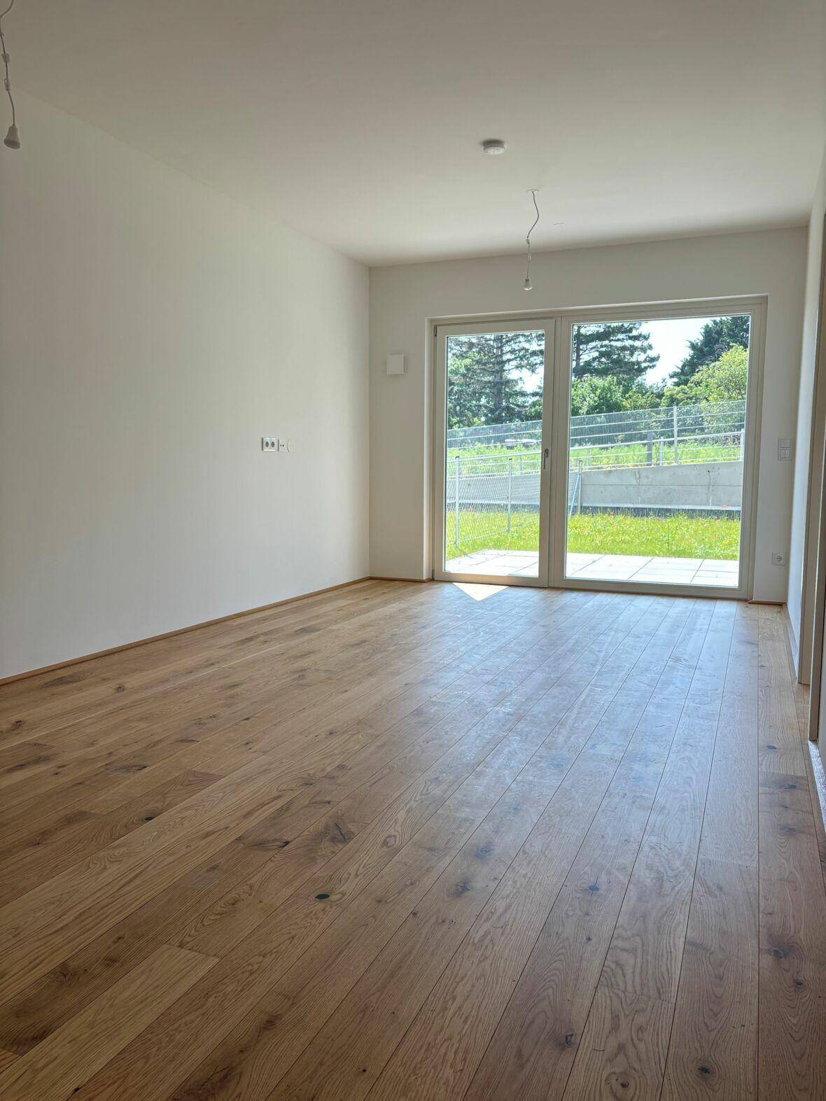 Helles Zimmer mit Holzboden und Zugang zu einer Terrasse mit Blick ins Grüne.