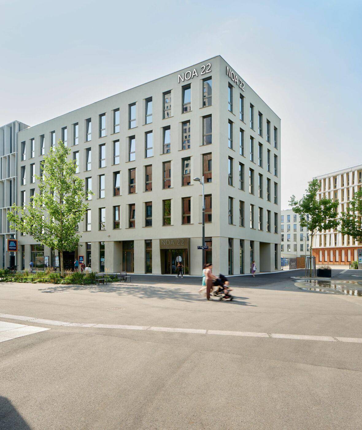 Modernes Geschäftsgebäude "NOA 22" an einem sonnigen Tag, umgeben von einer belebten städtischen Umgebung.