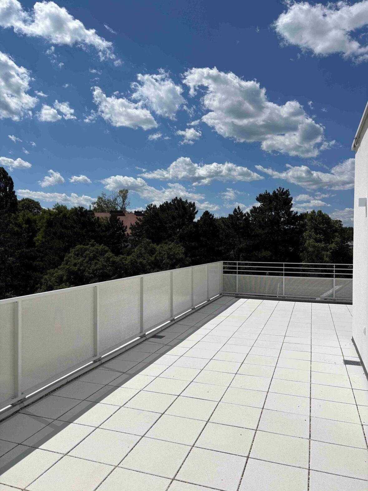 Geräumige, geflieste Dachterrasse mit weißem Geländer und weitem Blick ins Grüne.