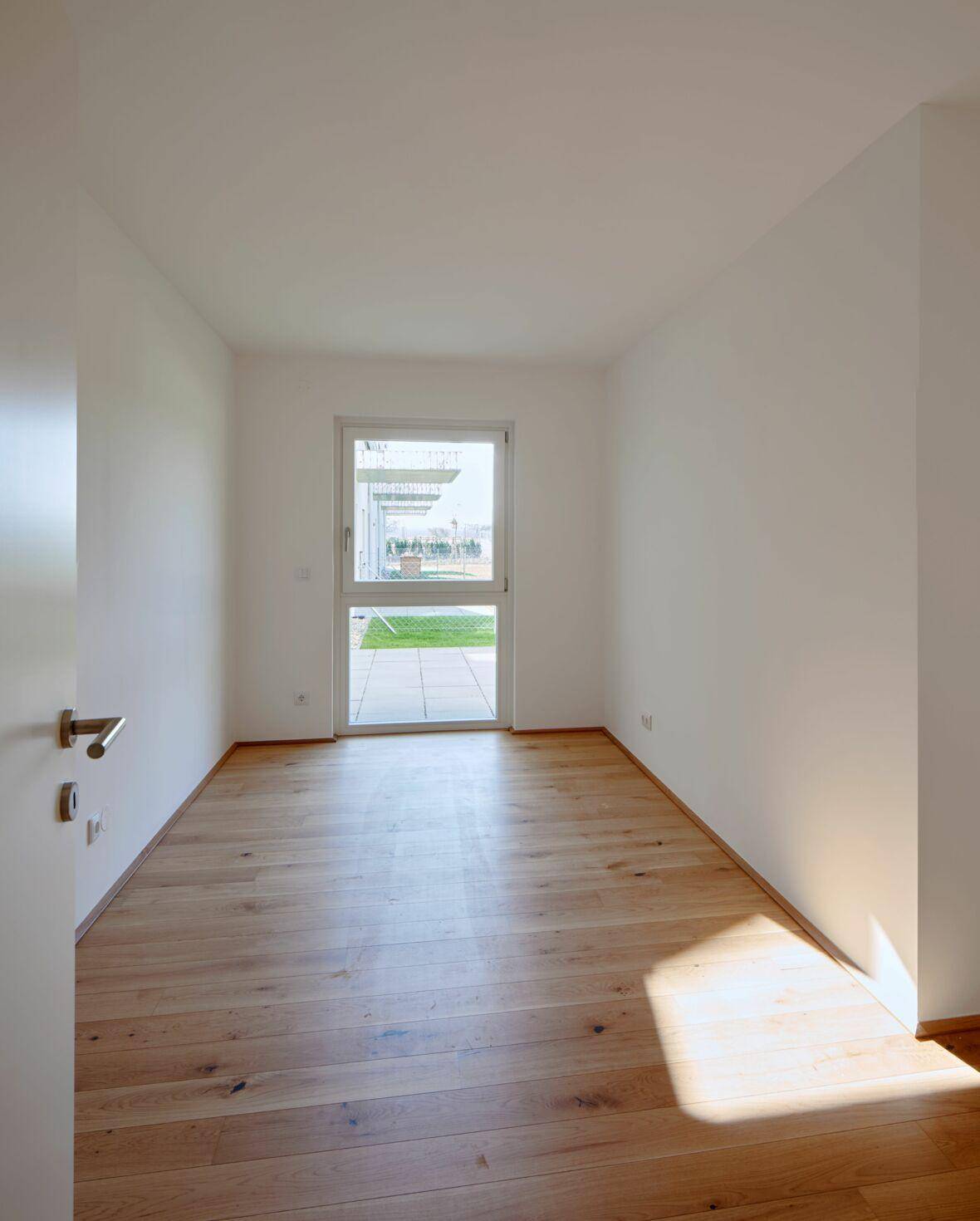 Kleiner, heller Raum mit Holzboden und einer Tür, die direkt in einen grünen Außenbereich führt.