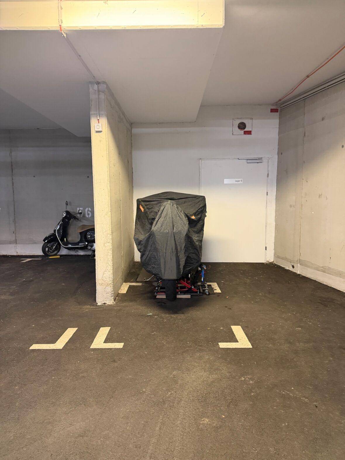 Tiefgaragenstellplatz mit Markierungen und einem abgedeckten Fahrzeug.