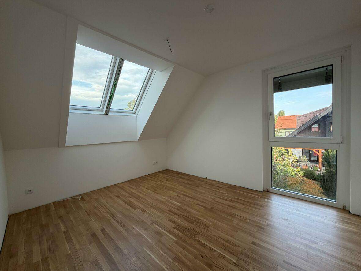 Helles Zimmer im Dachgeschoss mit Parkettboden, Fenster und zwei Dachfenstern.