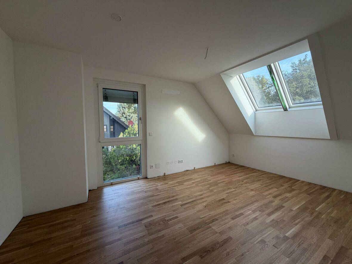 Lichtdurchflutetes Zimmer mit Parkettboden, Dachschräge und Blick ins Grüne.