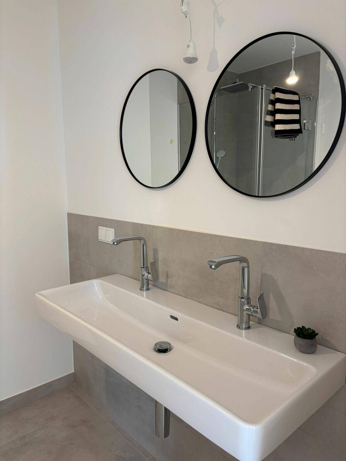 Modernes Badezimmer mit Doppelwaschbecken, zwei runden Spiegeln und einer begehbaren Dusche.