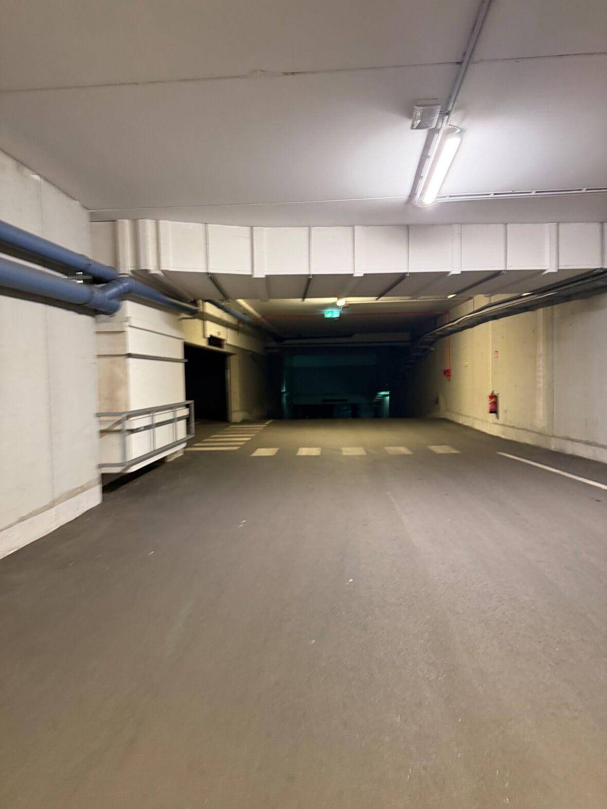 Langer Gang in der Tiefgarage mit Beleuchtung und blauen Rohren an der Decke.