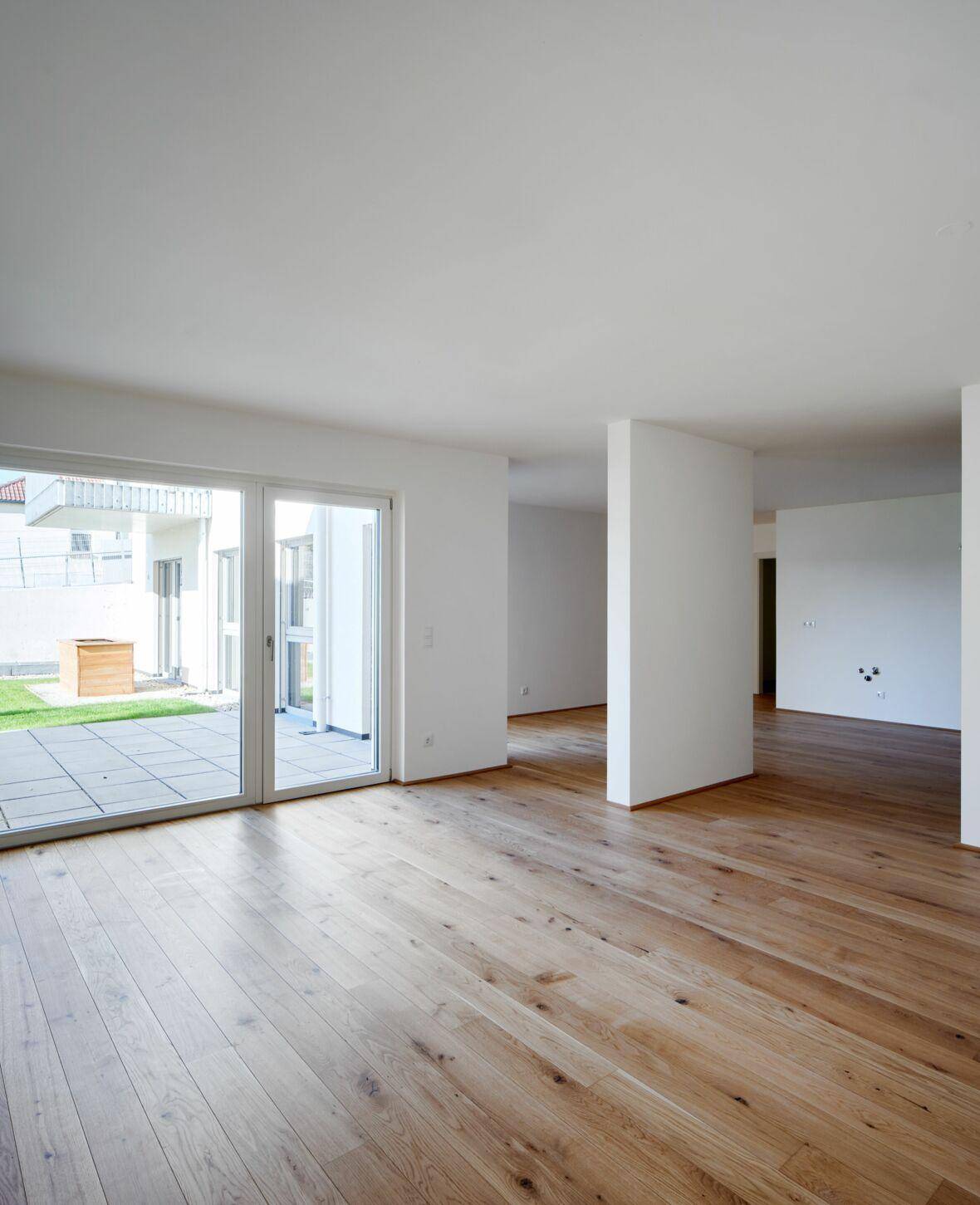 Geräumiges, helles Wohnzimmer mit Eichenparkett und Zugang zu einer Terrasse mit kleinem Gartenbereich.