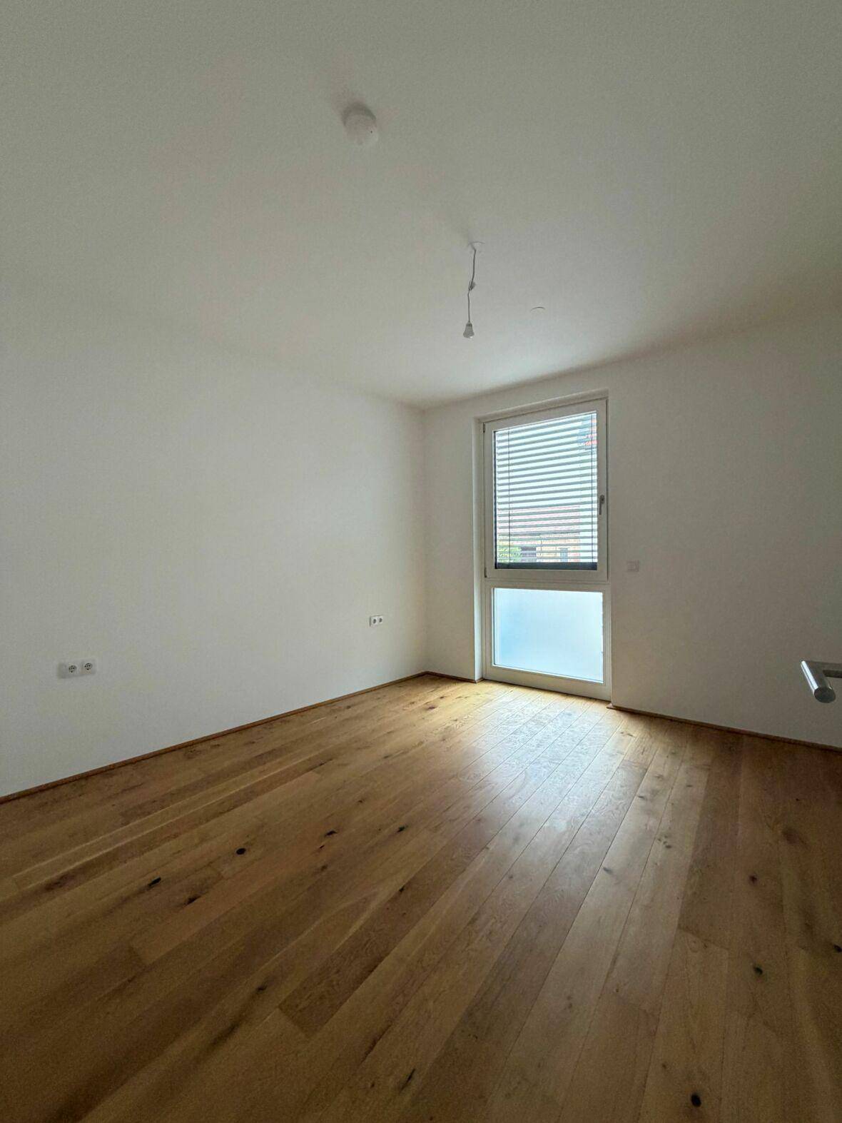 Heller Raum mit Holzboden und einem Fenster mit Jalousien, bereit zur individuellen Gestaltung.
