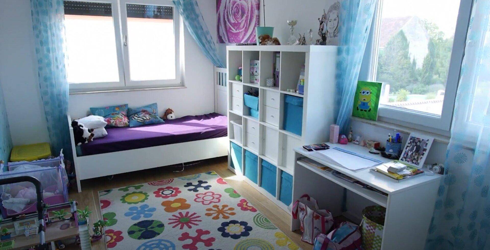 Farbenfrohes Kinderzimmer mit Bett, Schreibtisch und großem Fenster, das eine grüne Aussicht bietet.