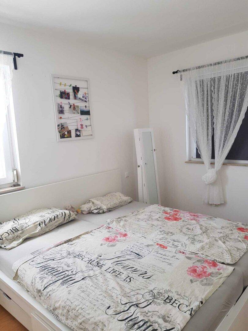 Helles Schlafzimmer mit Doppelbett und großen Fenstern, die viel Tageslicht hereinlassen.