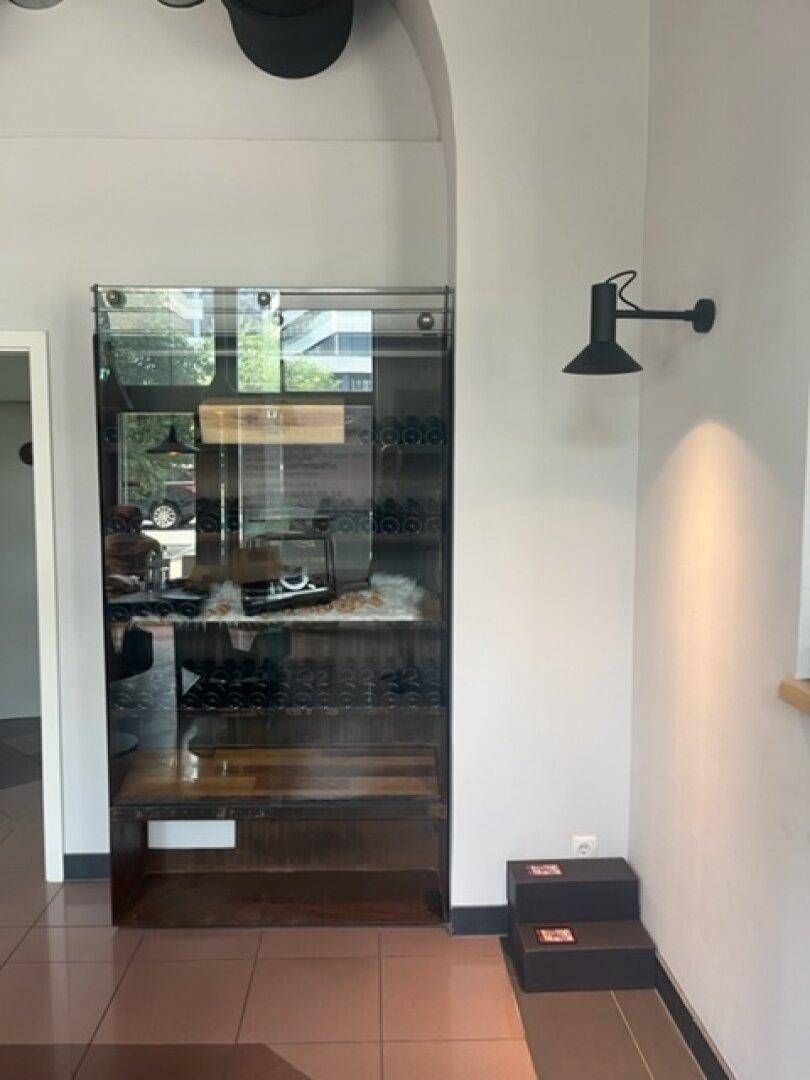Elegante Vitrine mit Glasfront und Holzregalen, beleuchtet von einer Wandleuchte, in einem hellen Raum.