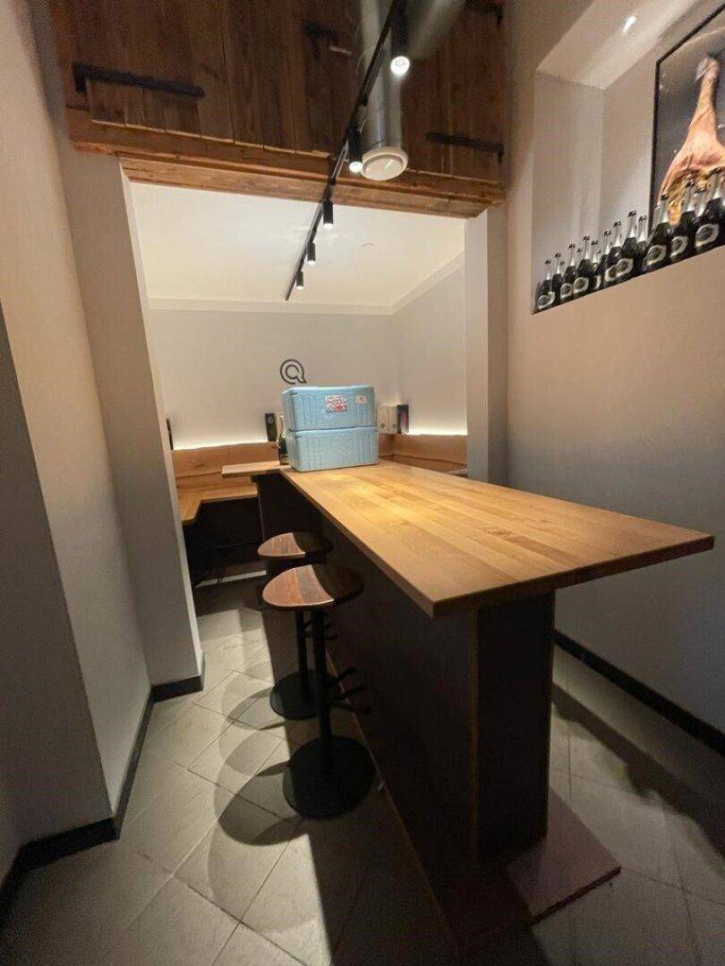Gemütlicher Sitzbereich mit Holztisch, Hockern und einer rustikalen Holzverkleidung an der Wand.