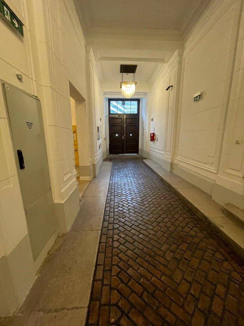 Langer Eingangsbereich mit Ziegelpflasterboden, hohen Wänden und einer eleganten Deckenleuchte.