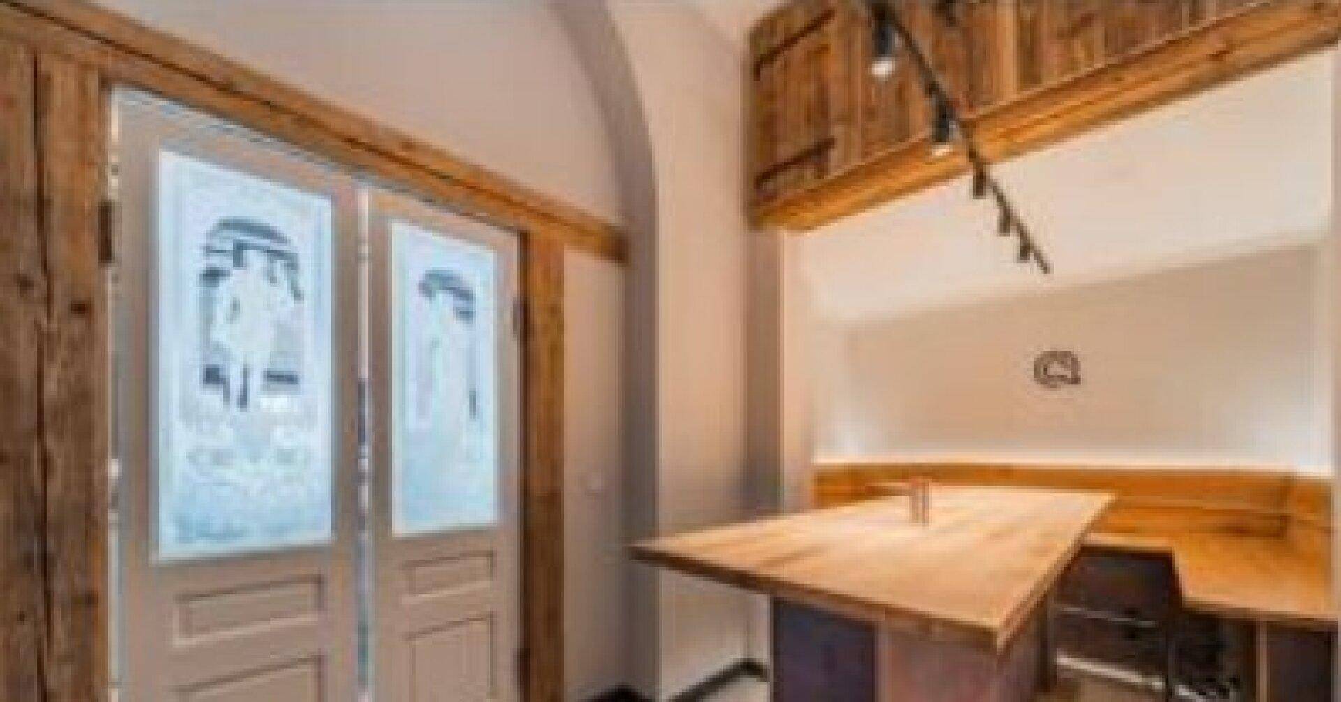 Kleiner, intimer Sitzbereich mit Holztisch und Bänken, umrahmt von rustikalen Holzelementen und einer Wandleuchte.