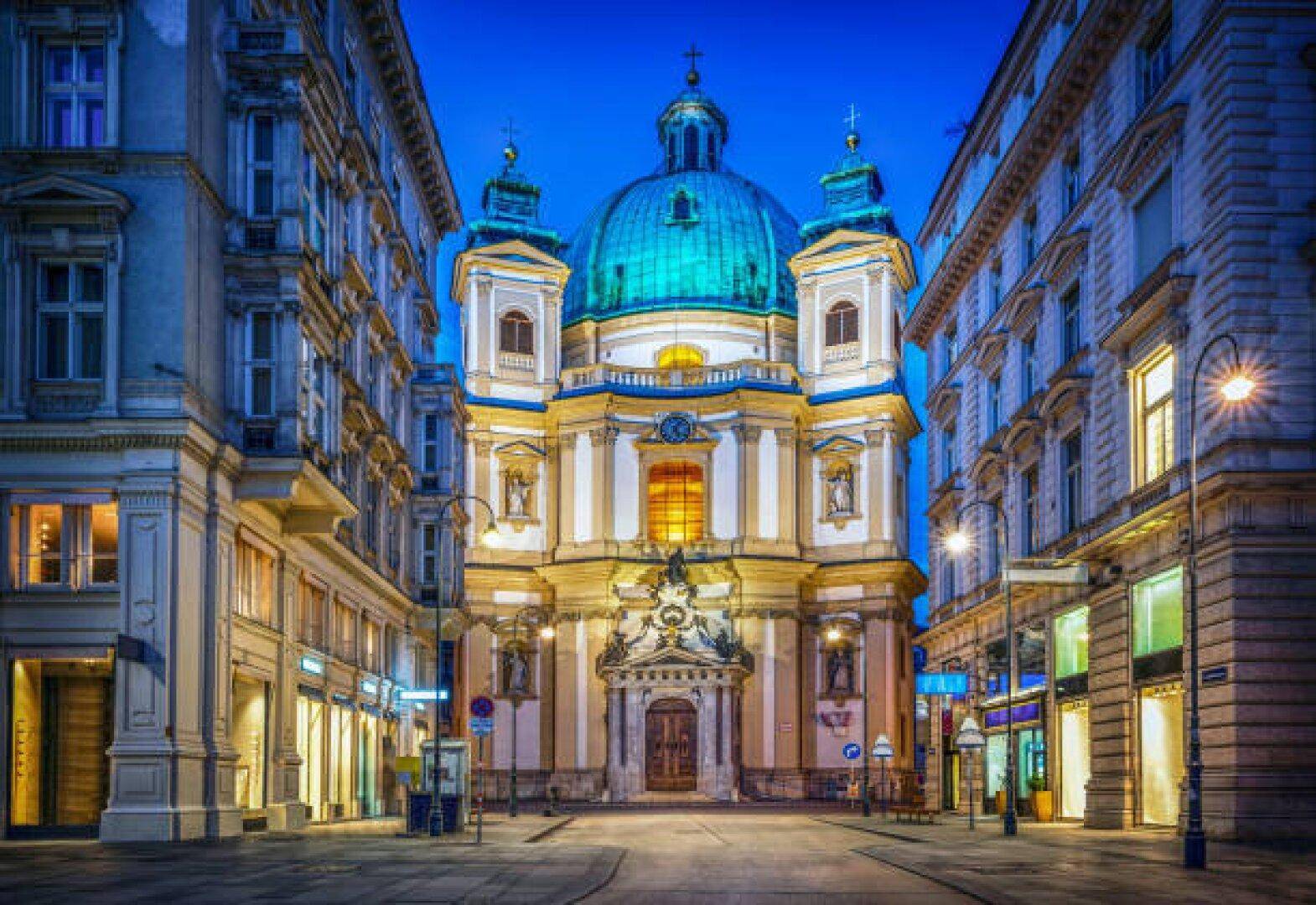 Nachtaufnahme einer prächtigen Barockkirche mit leuchtenden Fenstern, umgeben von beleuchteten Stadtgebäuden.