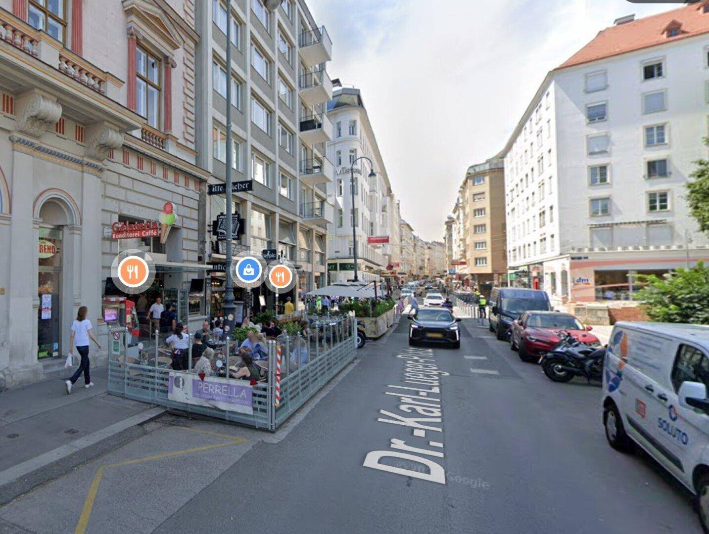 Belebtes Stadtbild mit Geschäften, Restaurants und einer Außenterrasse entlang der Dr.-Karl-Lueger-Straße.