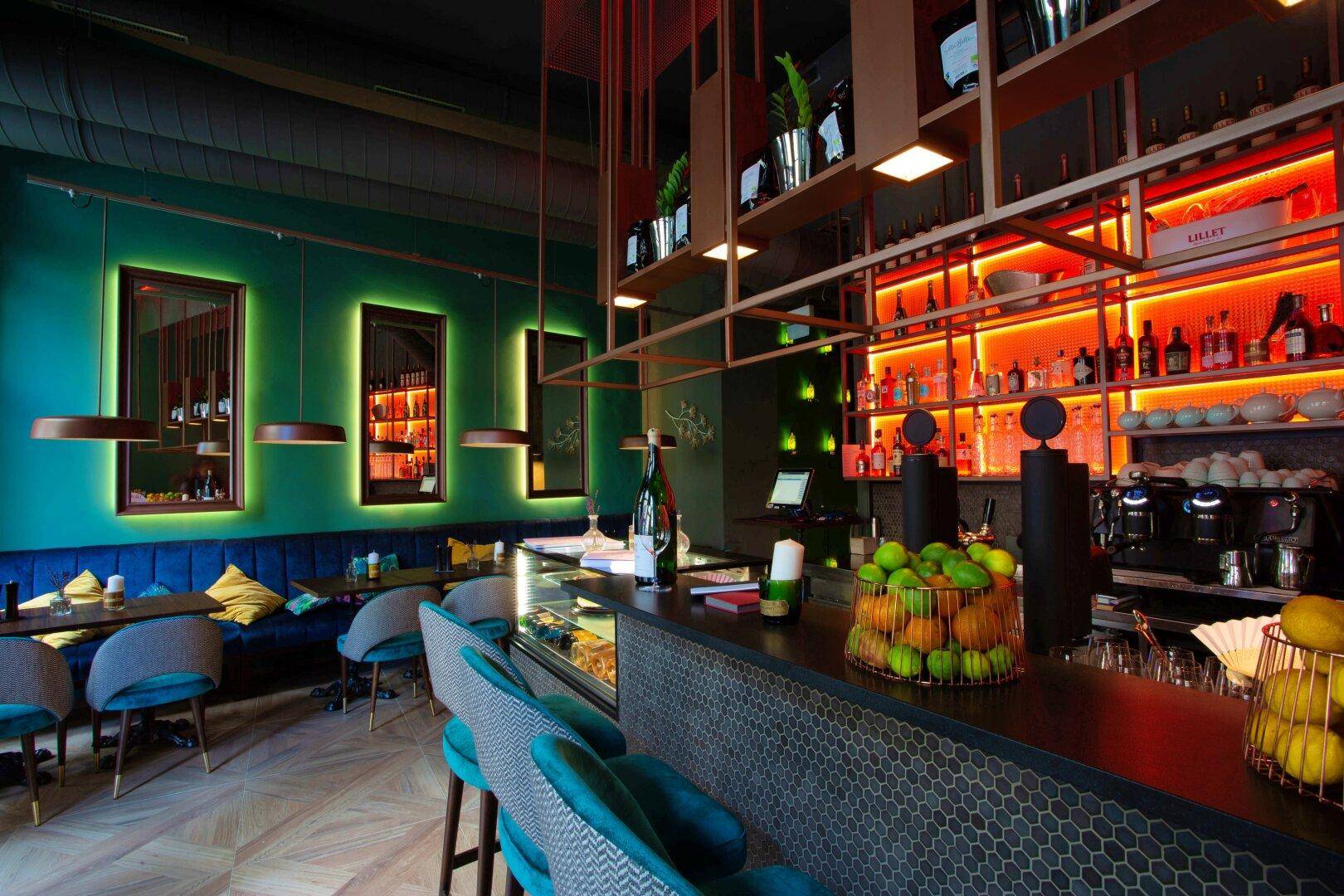 Stilvolle Bar mit leuchtenden Regalen, dunkler Theke und passenden Hockern, ergänzt durch den Restaurantbereich im Hintergrund.
