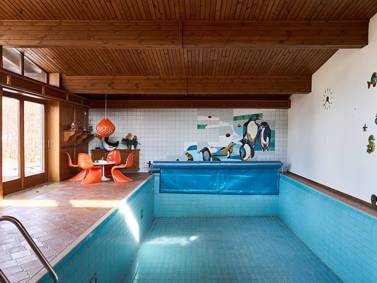 Geräumiger Innenpoolbereich mit gefliestem Becken, Holzdecken und retro Wanddekoration.