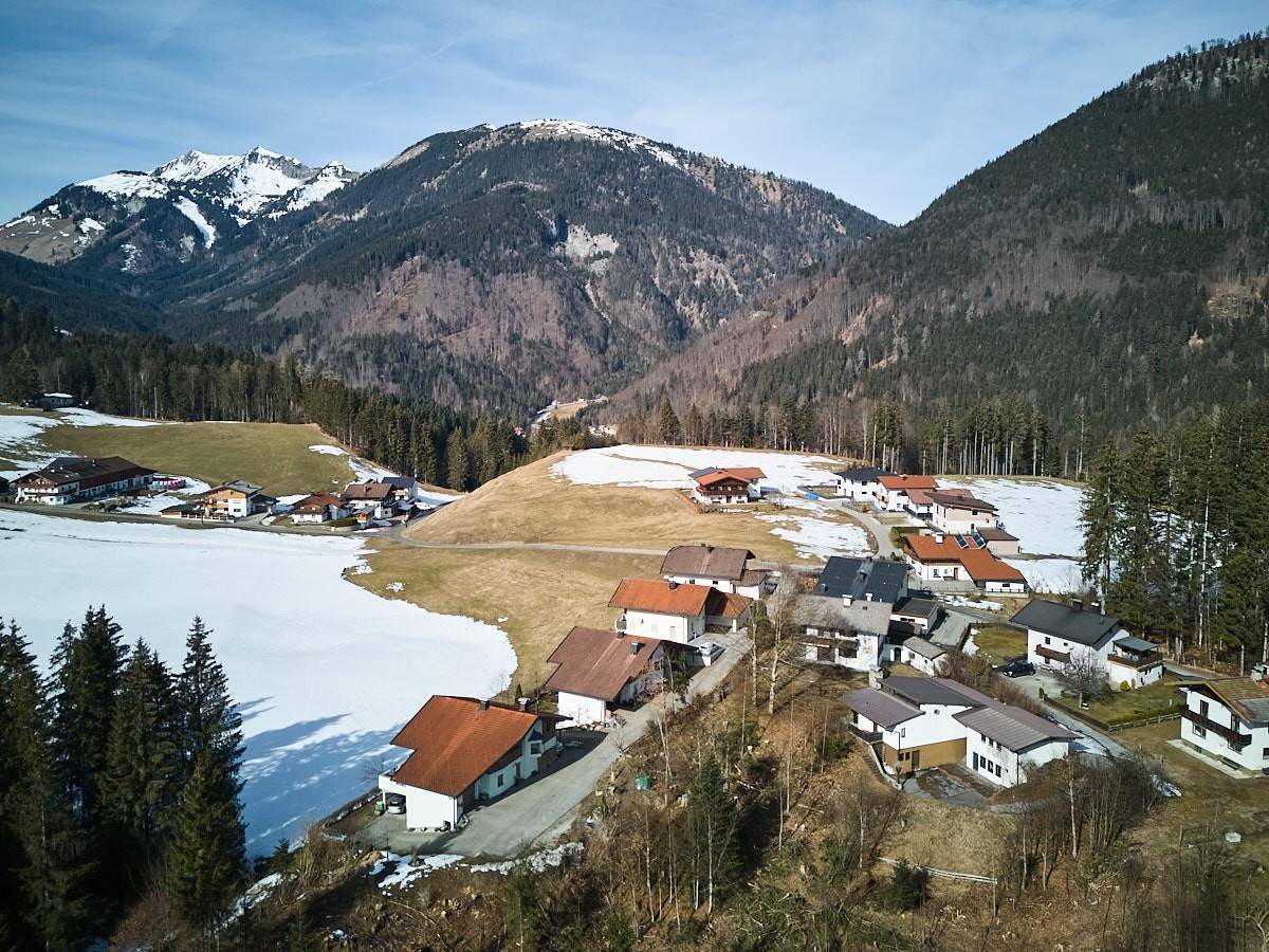 Weitläufige Luftaufnahme einer Siedlung in einer verschneiten Berglandschaft mit vielen Häusern und Wäldern.