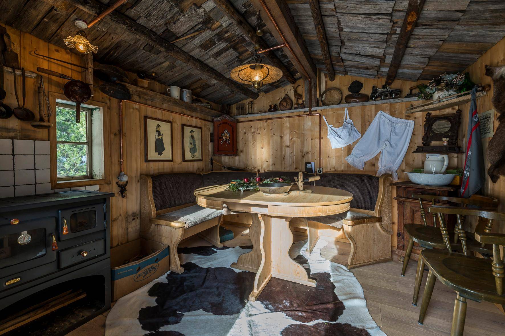 Uriges Esszimmer in einer Holzhütte mit Holzbänken, traditionellem Ofen und rustikaler Einrichtung.