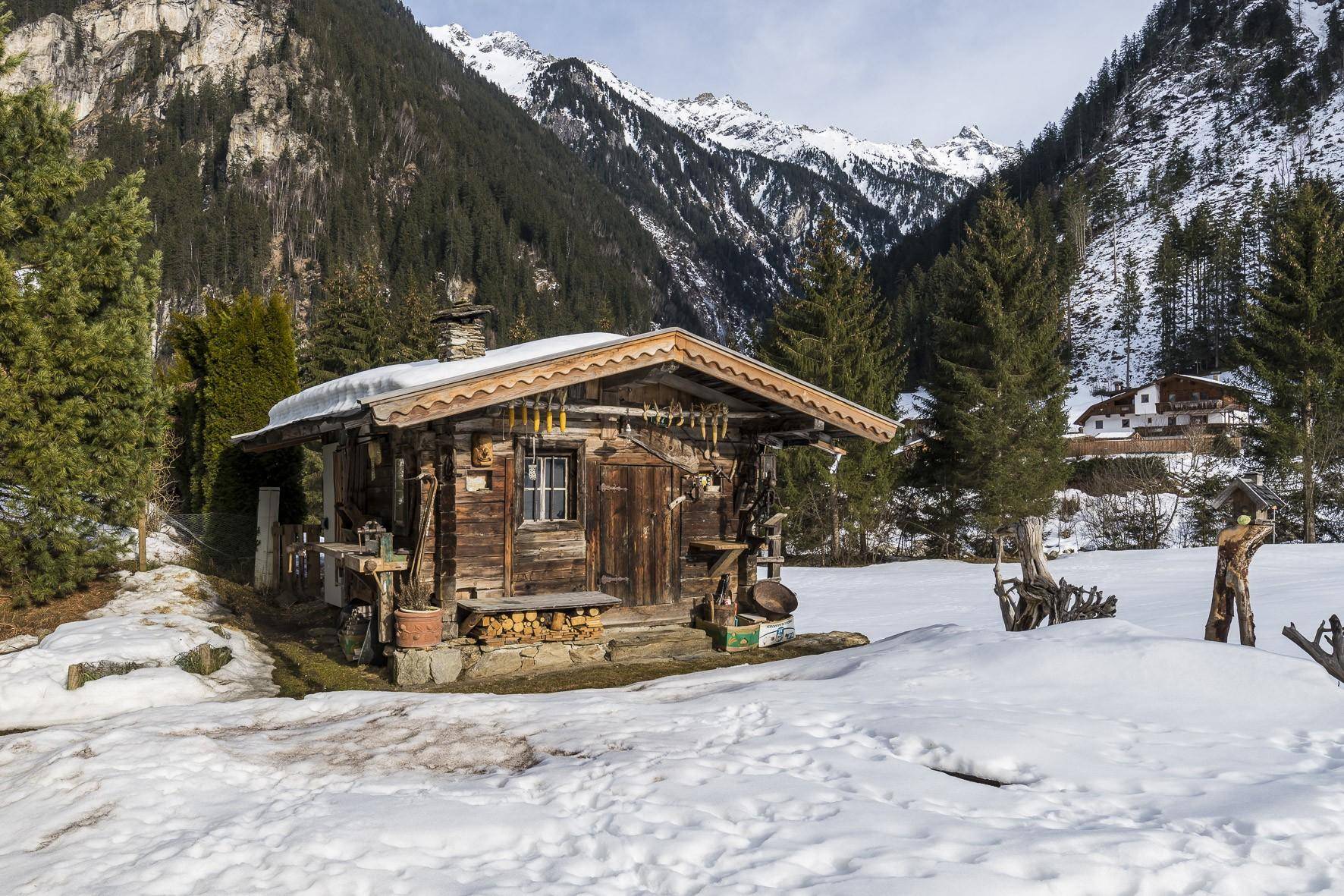 Charmante Holzhütte im Schnee, umgeben von Bergen und Bäumen, mit rustikalen Details.