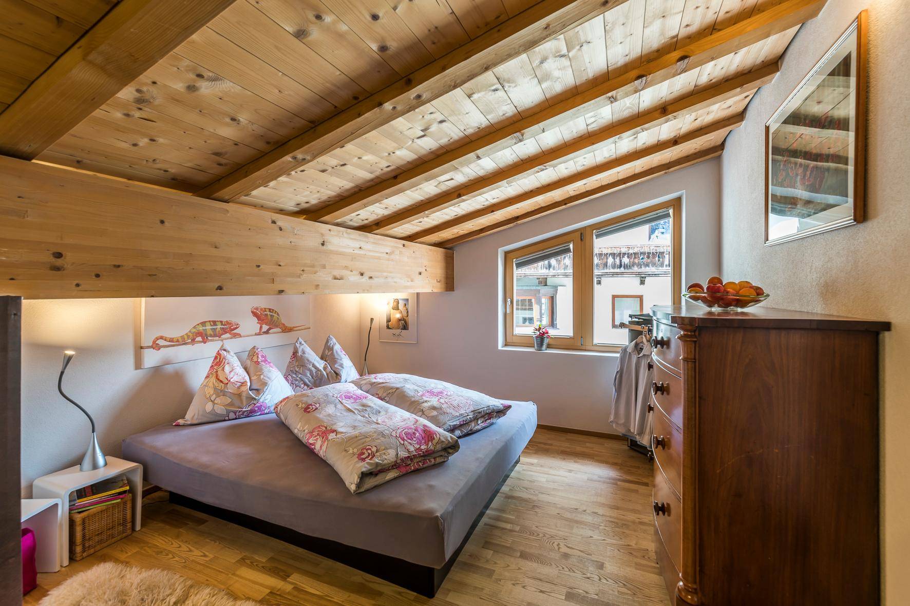 Helles Schlafzimmer im Dachgeschoss mit Holzbalkendecke, Holzboden und Blick auf die Umgebung.