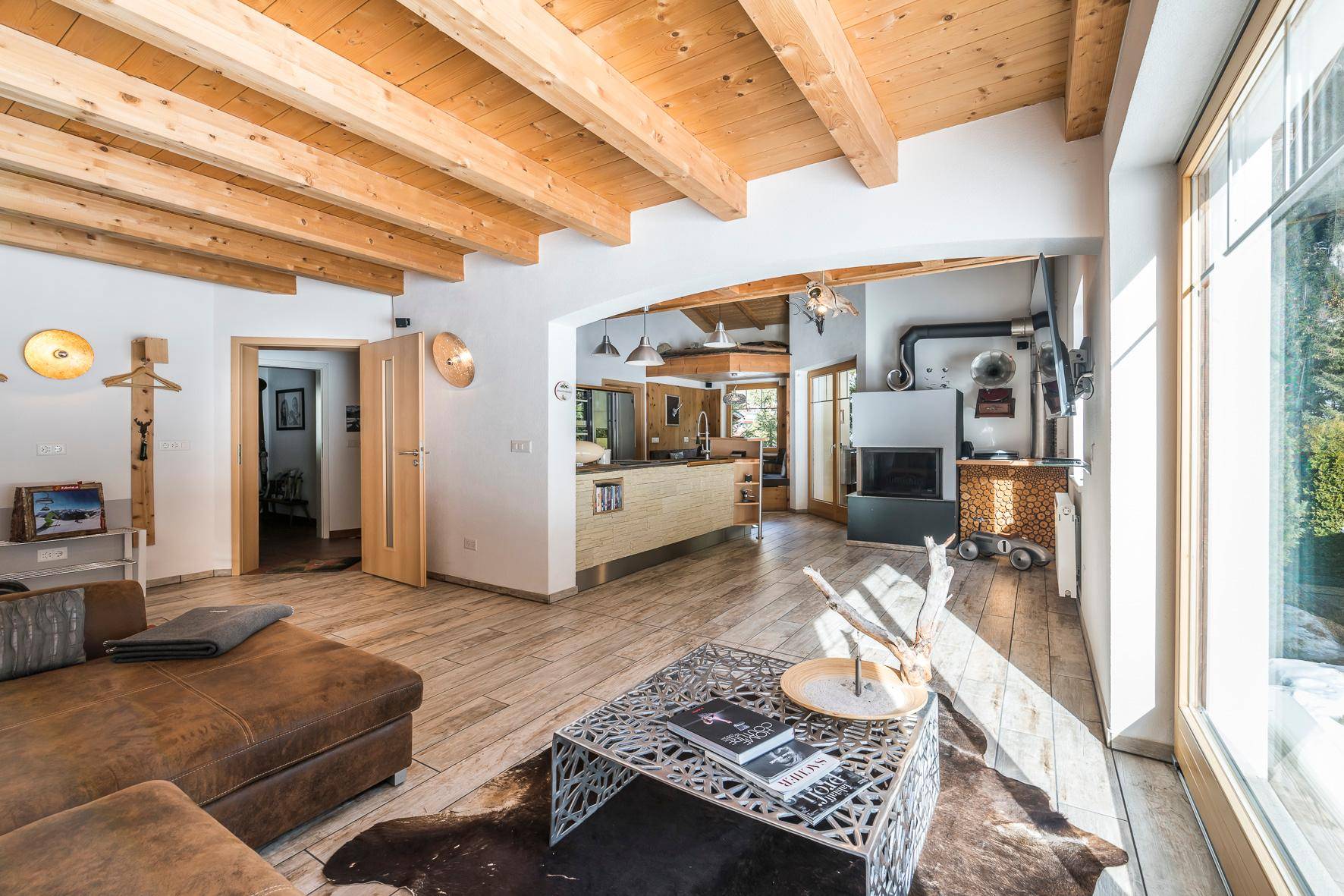 Gemütliches Wohnzimmer mit Holzbalkendecke, Kamin und großen Fenstern mit Blick auf die verschneite Landschaft.