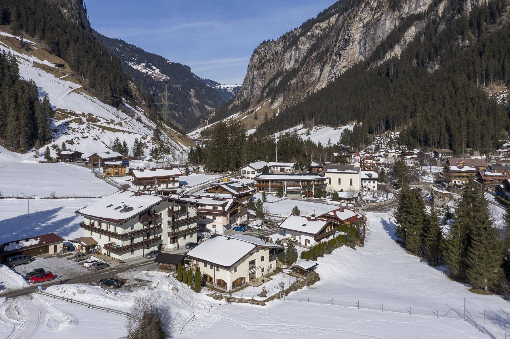 Weitläufige Ansicht eines idyllischen Bergdorfes, umgeben von schneebedeckten Hängen und alpiner Landschaft.