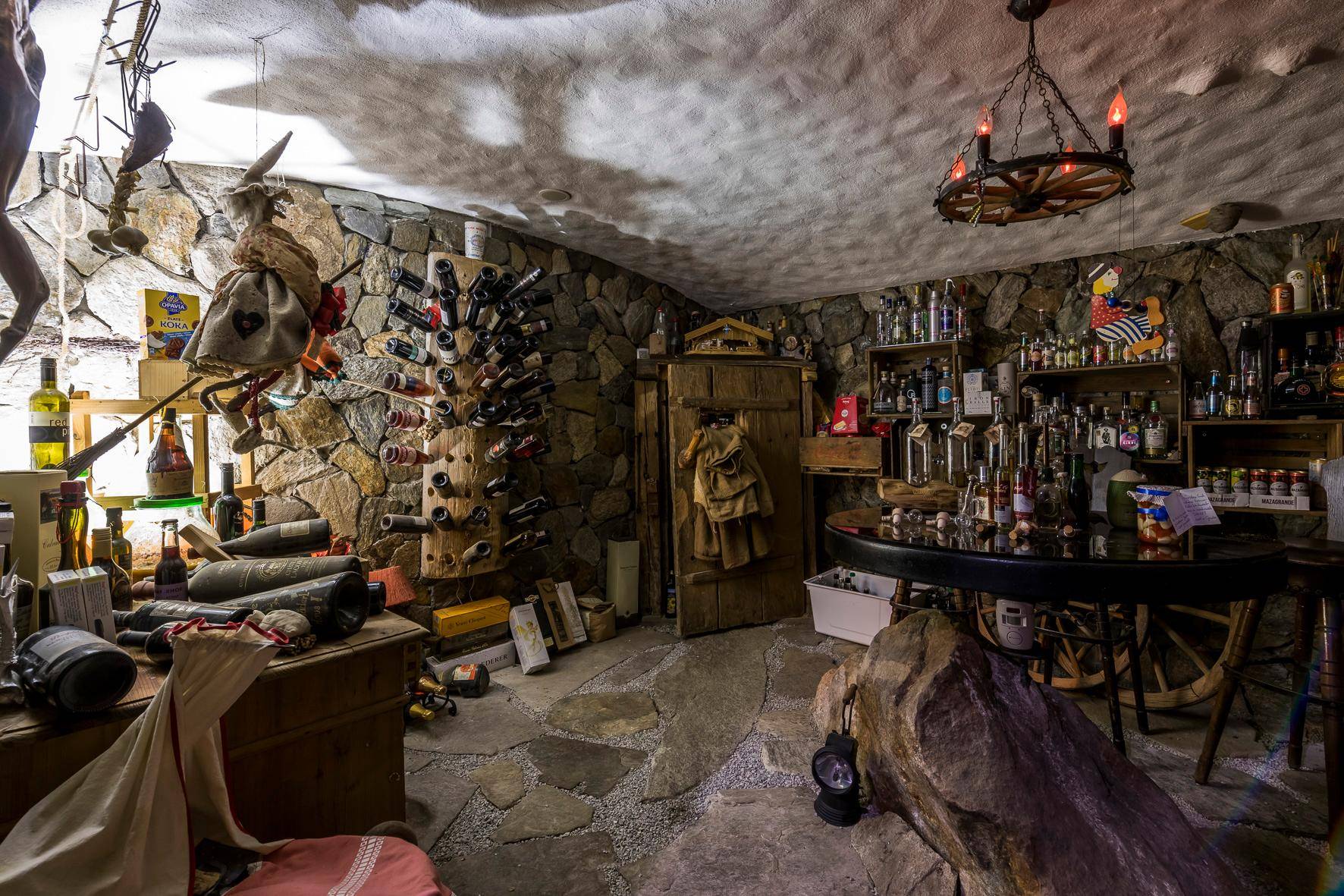 Rustikaler Weinkeller mit Steinwänden, Holzmöbeln und einer großen Auswahl an Flaschen.