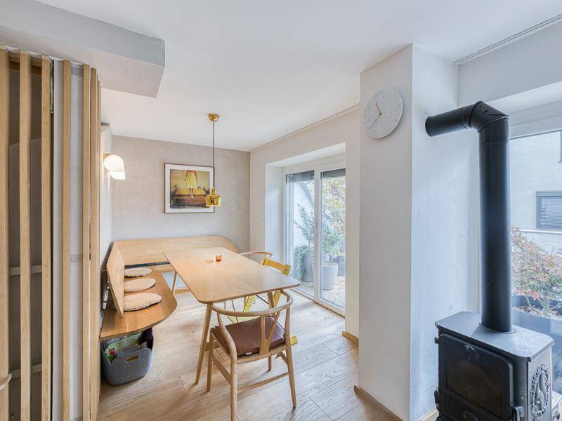 Gemütlicher Essbereich mit Holztisch, Sitzbank und Kaminofen neben großen Fenstern.
