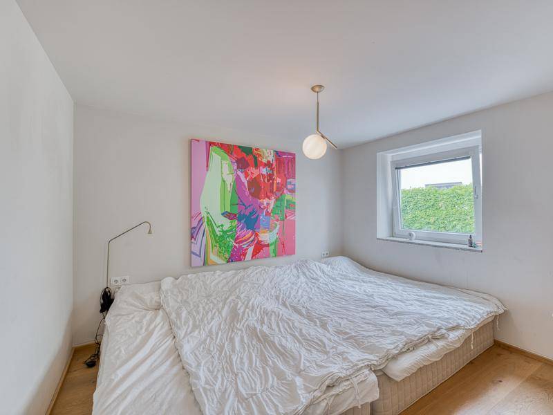 Schlafzimmer mit großem Bett, Holzboden und einem Fenster mit Blick ins Grüne.