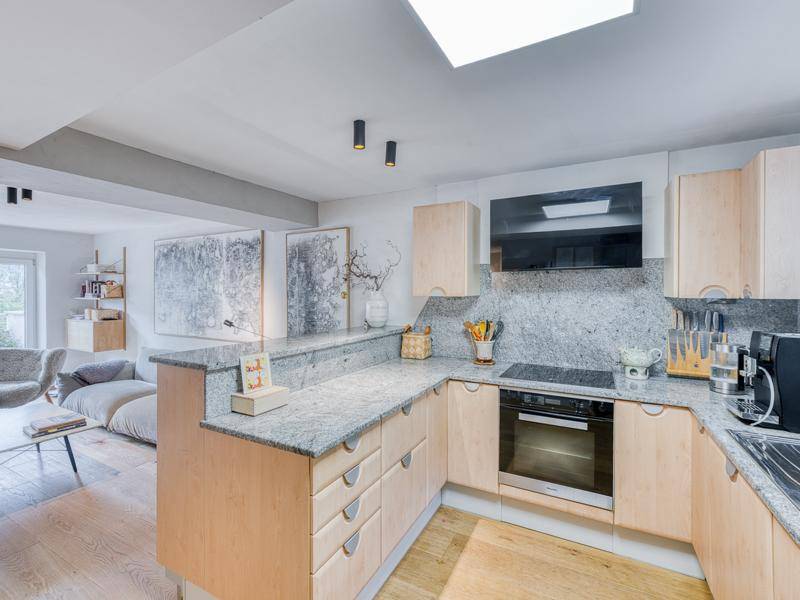 Helle Küche mit Holzschränken, Granitarbeitsplatten und offener Verbindung zum Wohnbereich.